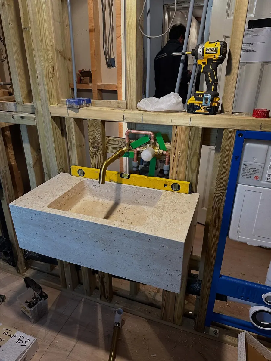 A stone basin being fitted to a new stud wall, with a spirit level and drill on top