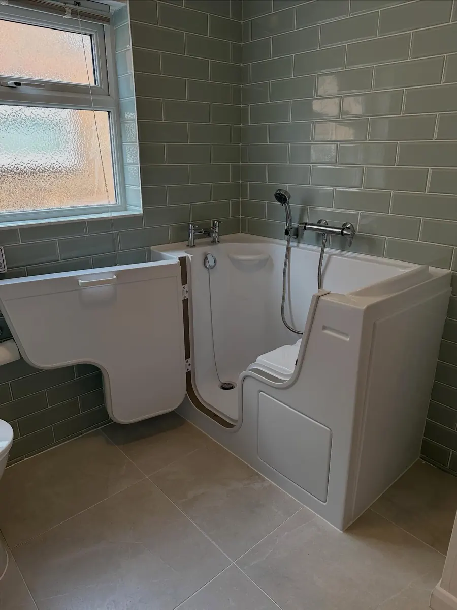 A walk-in bath with a door in a bathroom with sage green metro tiles