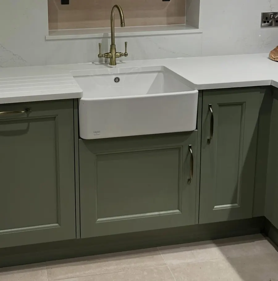 A white Belfast sink with a brass tap in a sage green shaker kitchen