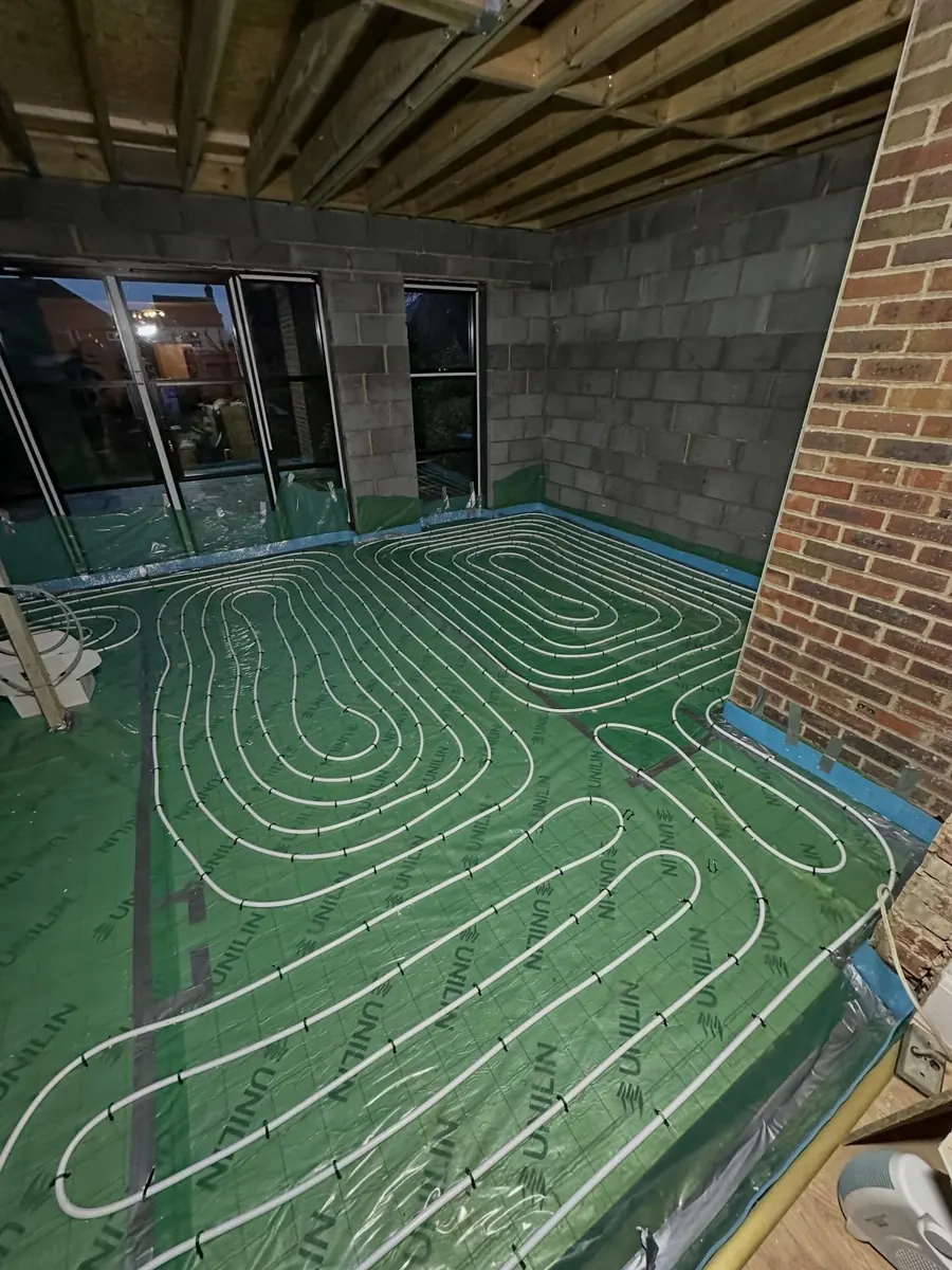 Underfloor heating pipe loops laid on insulation in a room with exposed brick and timber joists